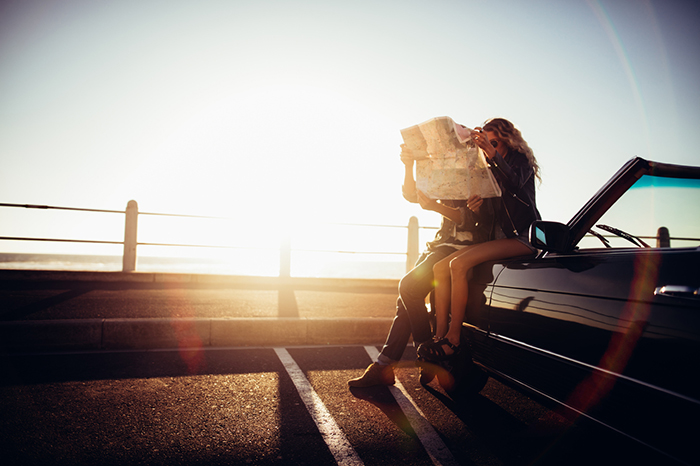A man and woman consult a map outside their car as the sun sets