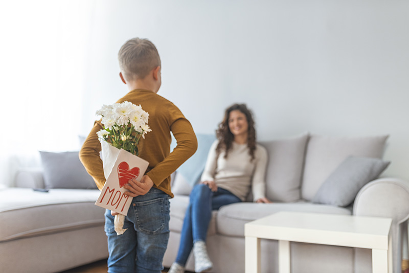 Boy holding flowers and a card for his mom on mother's day