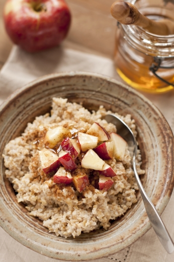 Rustic handmade pottery bowl filled with oatmeal made from steel cut oats. Garnished with apples, honey, and cinnamon.