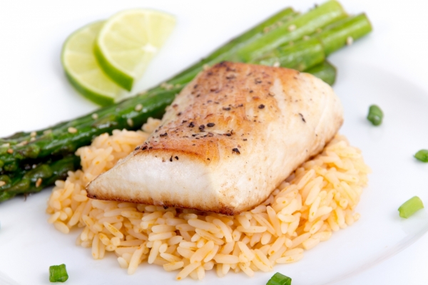 A broiled white fish on a bed of rice with a side of asparagus