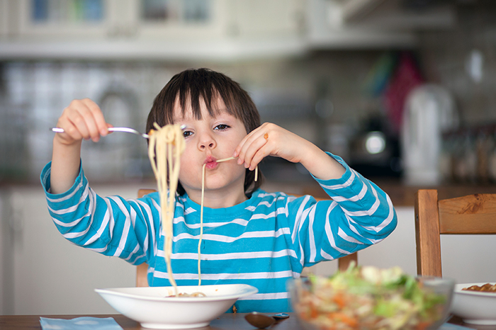 A cute little boy eating chicken spaghetti at home