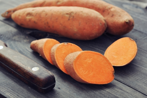 Several sweet potatoes on a cutting board with some slices and a knife