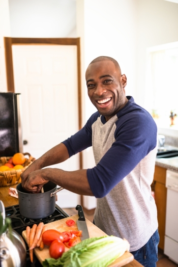 A smiling, happy man standing in the kitchen and preparing food