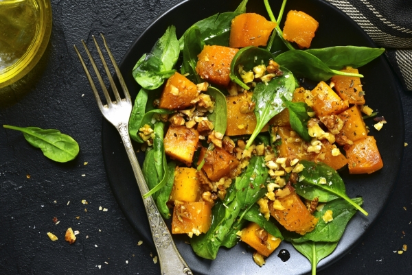 Roasted pumpkin salad with spinach and walnut on a black plate on a stone background.Top view.