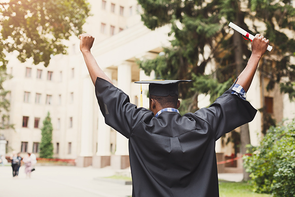 Young woman on her graduation day in university holding up diploma.