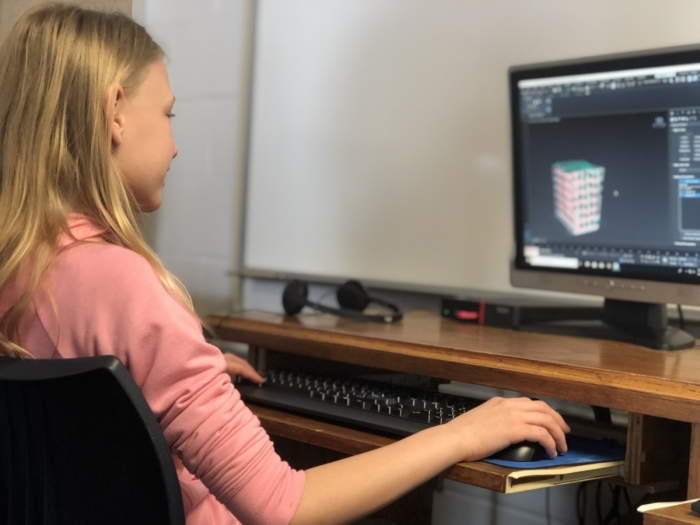 A young female blond student works on a 3D design project at her computer. 