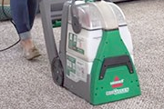 Someone using the BISSELL® Rental Big Green Deep Cleaning Machine® to clean the carpet.