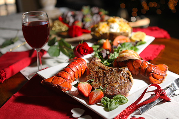 An elegant dinner of steak and lobster with wine and roses.