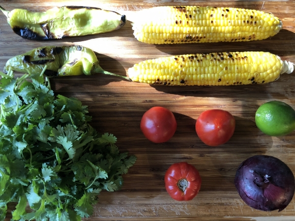 Salsa ingredients on a wooden background (corn, hatch chile, cilantro, tomatoes, onion, and lime)