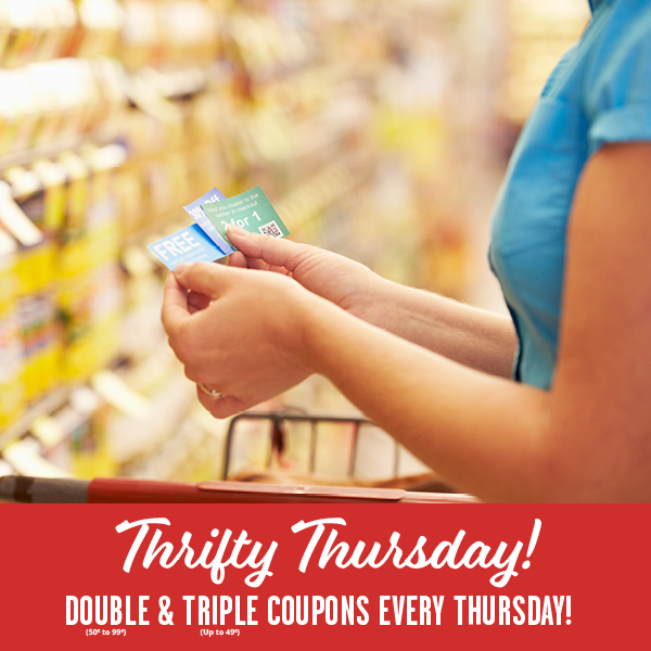 A woman standing in a grocery aisle looking at a handful of coupons.